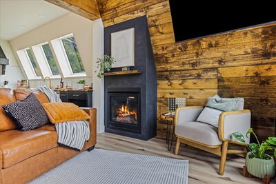A modern A-frame cabin called the Perrine Hideaway with dark exterior siding, large glass windows, and a rugged canyon backdrop, blending nature with contemporary design.