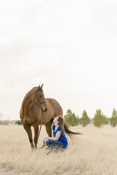 Megan Brincks of Midland Texas kneels in front of Quest, her bay Off the Track Thoroughbred  in a field near On The Mark Equestrian