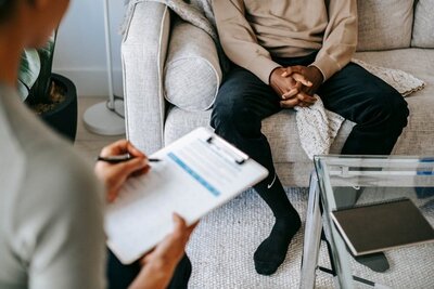 A close up picture of two people in a therapy session with therapist writing down notes