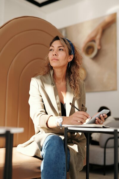 A woman sitting at a desk and writing in a notepad while looking into the distance