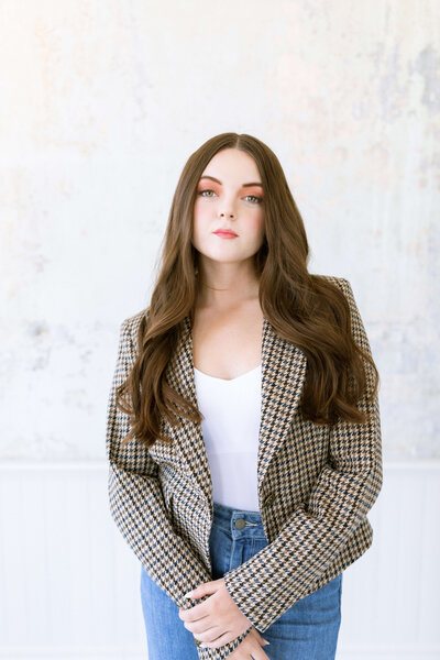 brunette girl with bright lipstick and a plaid blazer and white shirt and blue jeans