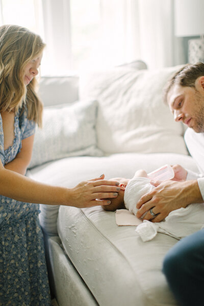 A mother and father sitting with their newborn baby on a couch while the dad feeds the baby a bottle