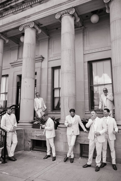 Bride in white dress and veil hugs groom in light suit under a tree, smiling warmly. The setting is outdoor, evoking romance and joy.