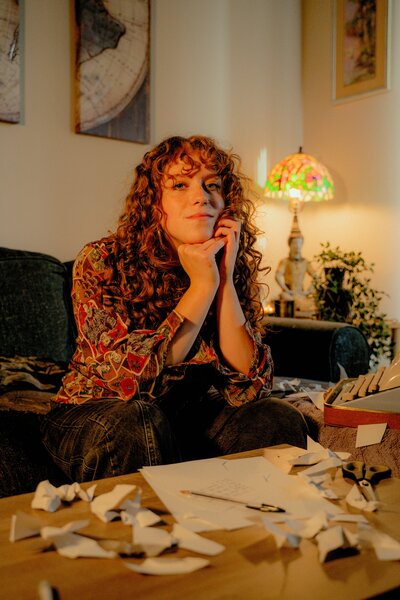 picture of Angela Morano looking at the camera sitting on a couch with a table and pen and paper in front of her 