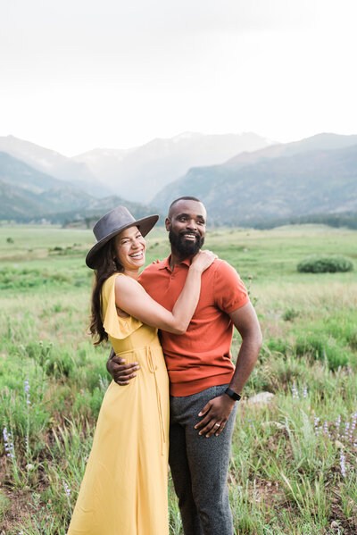 outdoor colorado engagement photos with  bride and groom walking across a field in bright yellow dress and the groom in an orange top