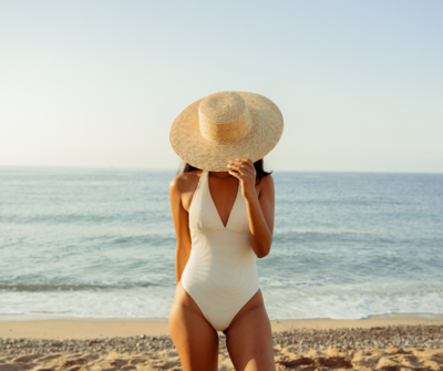 Woman on the beach with sunhat in front of face, luxury travel concierge