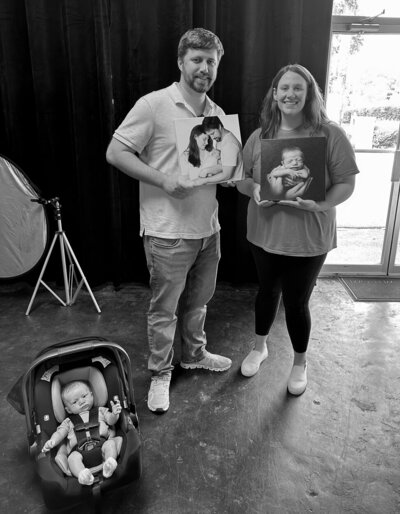 black and white image of parents with newborn holding canvas art pieces at Insley  portrait studio charlotte nc