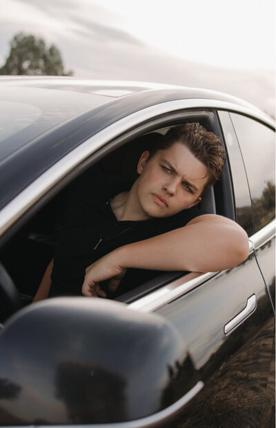 Senior session of a boy in his car with a neutral face, not looking at the camera.