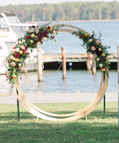 Wedding ceremony arch decorated with blush and burgundy wedding flowers. Wedding in St. Michaels, Maryland. Artistic floral design for waterfront wedding venues in Maryland.