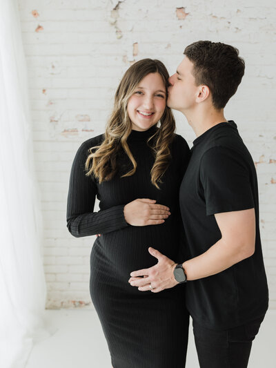 husband and pregnant wife in black maternity dress holding baby bump for studio maternity portraits cleveland maternity photographer