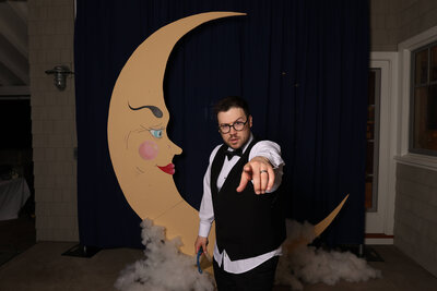 A man poses in front of a moon prop, representing props used with the Birdie Booth, a Eugene photo booth rental for wedding and events.