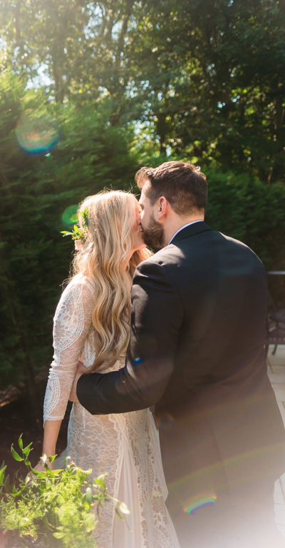 A bride with blond hair and her groom kiss in the sunlight