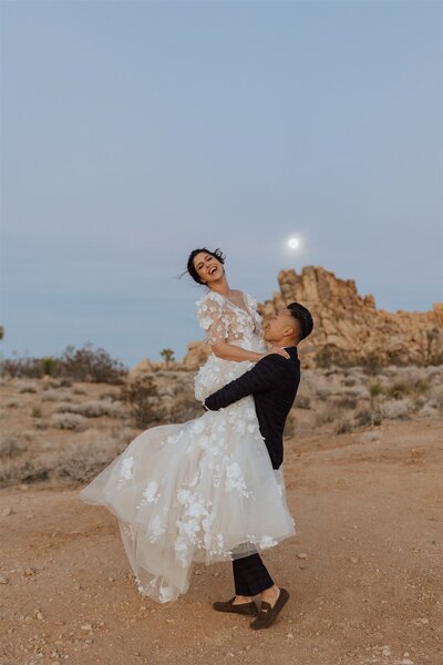 groom lifting and spinning bride with the moon shining in the sky