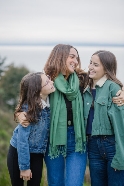 Three sisters smiling with each other in front of the Puget Sound in Seattle.
