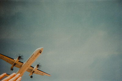 Looking overhead at a plane taking off with fingers in the bottom left of the shot