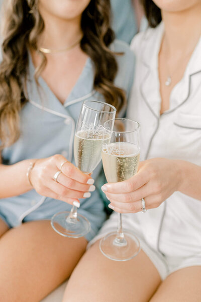 Bride and Bridesmaid in PJ's tipping champagne glasses towards each other during getting ready photos.
