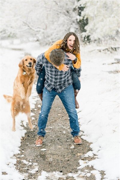 man and woman in snow with dog jumping