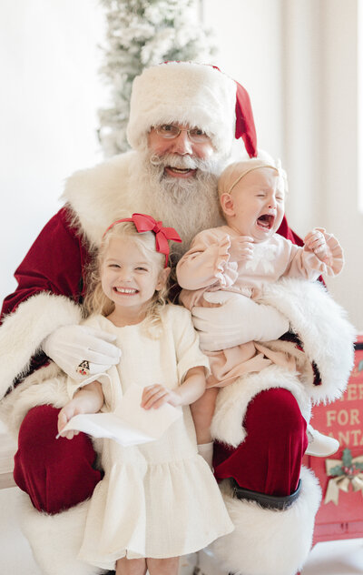 Two smiling children sitting with Santa Claus during a festive holiday mini session captured by a Kansas City family photographer.