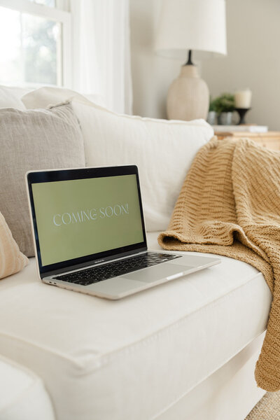 Macbook Pro sitting on a white couch displaying a coming soon sign