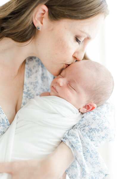 Mother kisses her newborn babies forehead during newborn portrait session