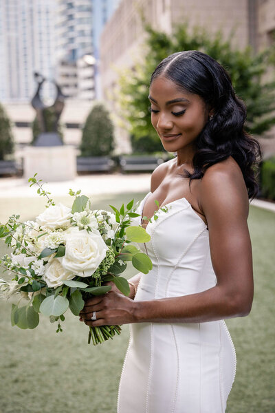 a bride in a wedding dress in a garden looking down towards her bouquet