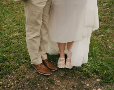 A bride and a groom standing next to each other showing off their shoes in Colorado. 