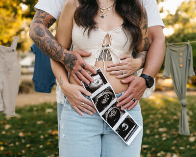 Picture of woman and man embracing with ultrasound placed in front of woman's stomach showing a baby.