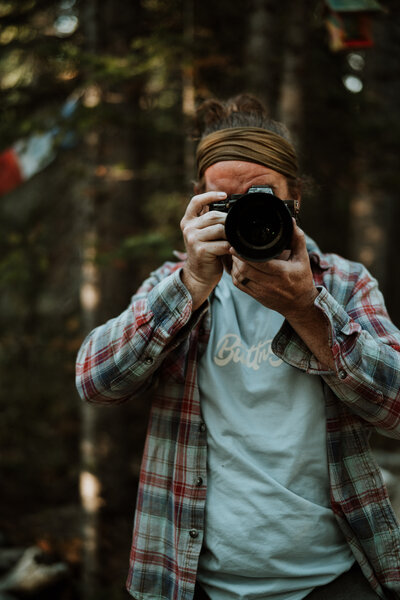 Videographer in plaid shirt captures wedding moments in Breckenridge forest.