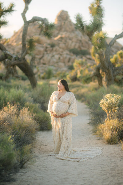 A mother-to-be in a delicate lace gown standing amid the desert landscapes of Joshua Tree National Park, captured in a refined editorial style by Elizabeth Kane Photography—serving Philadelphia, New York, and DC.
