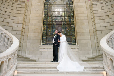 A wide photo of the bride leaning on the grooms shoulder on the stairs of the Old Courthouse in Cleveland