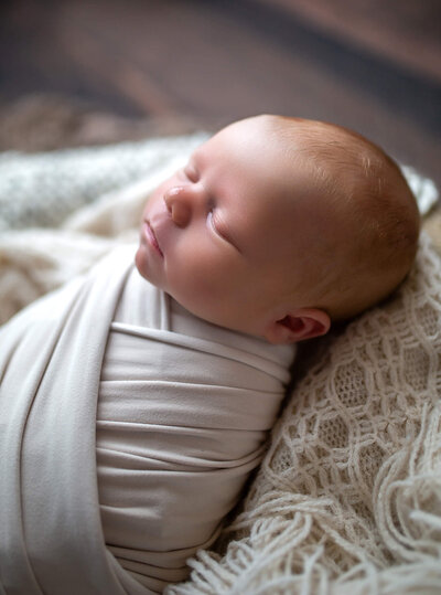 Simple neutral side view of baby's face wrapped in beige fabric 