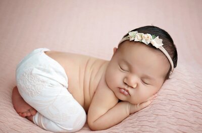 20 day old baby girl wearing a headband and sleeping on belly and wearing only a pair of pure white cotton pants.