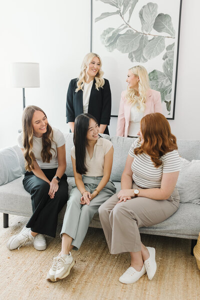 A group of allied health therapists laughing and engaging in a bright, modern studio during a branding photoshoot, showcasing their approachable and professional team dynamic.