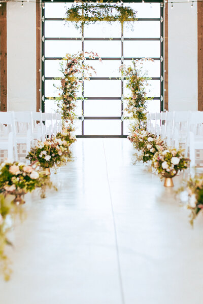 Wedding Aisle of White Barn Weddings Venue. Decorated with flowers and white chairs.