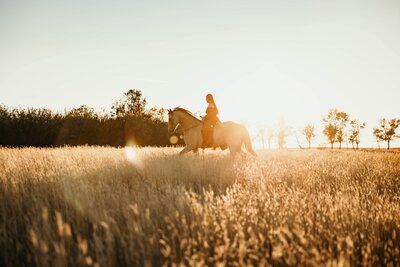 woman lopes horse through a grassy field in southern Alberta during an empowerment session 