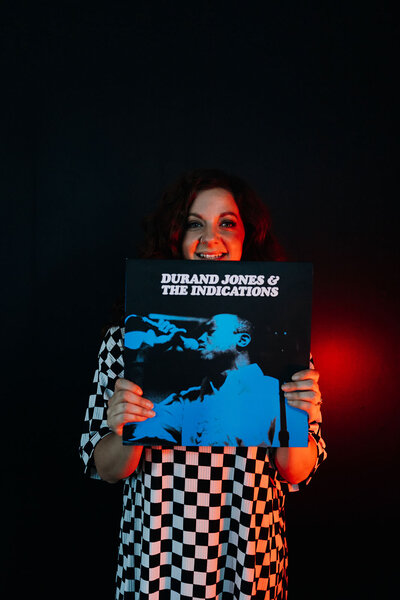 A woman smiling and holding up a vinyl record cover.