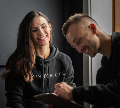 Personal Trainer and client sitting next to each other going over introductory questions before their personal training session at Train for Life Colllingwood Gym