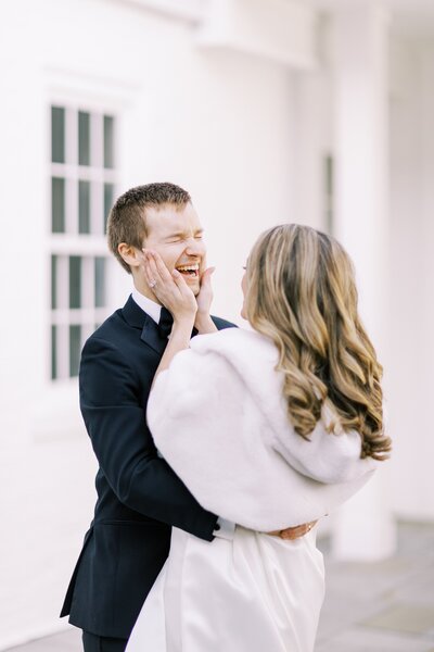 Bride holding groom's face in her hands laughing