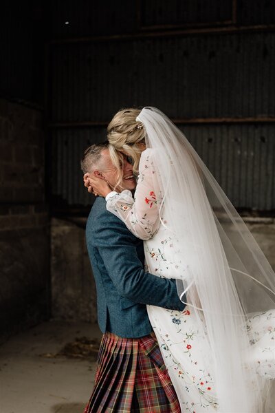 A lose photograph of a groom lifting a bride in an Aberdeenshire barn at their wedding. 