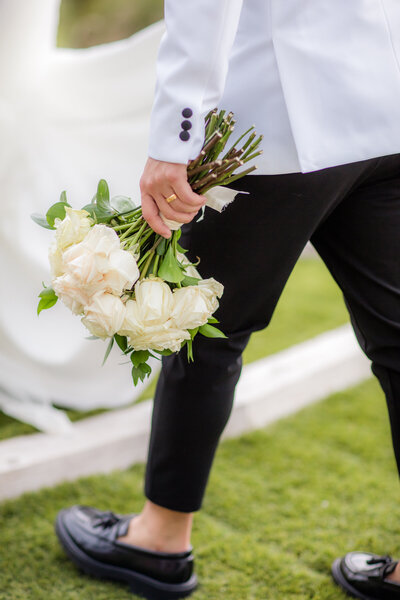 This image showcases a groom holding the brides bouquet. 