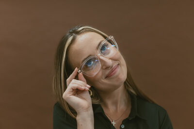 woman smiling with her head tilted while touching her glasses