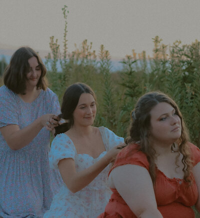 Three friends can be seen braiding each others hair as the sun sets in the bckground.