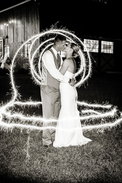 Couple kissing inside a swirl of sparklers outside the Wedding Barn at Evan's Orchard in Gerogetown, Kentucky.