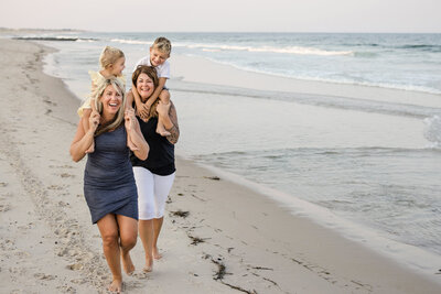 LGBTQ couple running on the beach with children laughing for photos at the Jersey shore.