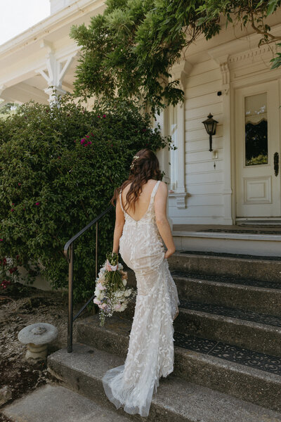 Bride Holding Gown and Bouquet walking up staircase