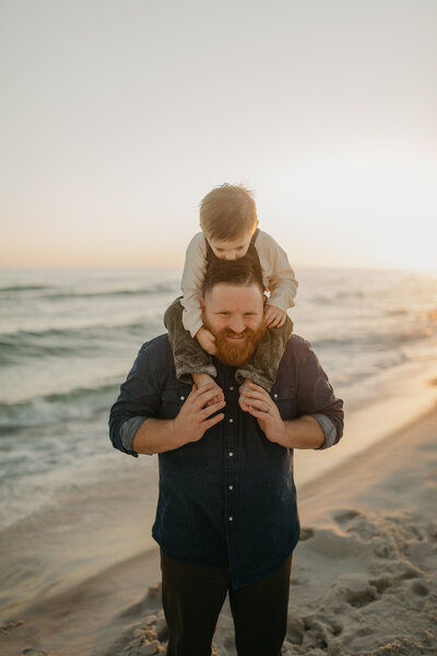 man with son on shoulders on beach