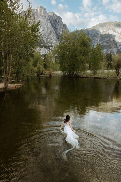Adventurous bride wading through river in wedding dress during Washington elopemen