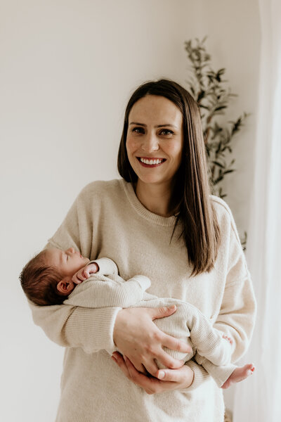 woman holding baby smiling at camera neutral colors