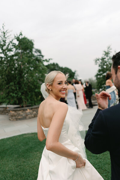 Photo of bride walking towards wedding guests looking back at the camera