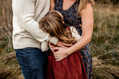 Detail shot of a mom and dad hugging their young daughter.